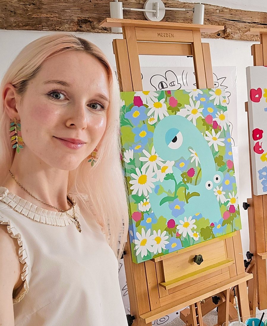 Tori Woolley smiling in her studio, with Pure Temptations and Floral Dopamine on easels behind her